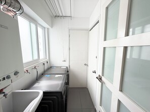 Ein schmaler Gang mit einem Fenster, einem Waschbecken und einer Tür mit satinierten Glasscheiben.