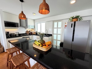 A modern kitchen with a central island, stainless steel appliances, and wicker pendant lighting. - BE ALOHA | Elegant Stay | 2 Blocks from the Malecón (Lima)