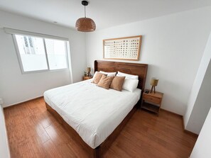 Un dormitorio con una cama grande, cabecera de madera, mesitas de noche, una lámpara colgante y una ventana.