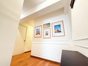 Ein Korridor mit Holzdielen, weißen Wänden und gerahmten Bildern an der Wand.