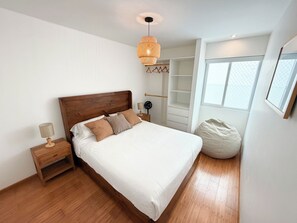 Ein Schlafzimmer mit einem hölzernen Bett, Nachttischen, einer Pendelleuchte, einem Kleiderschrank und einem Fenster.