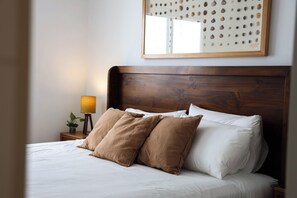 A neatly made bed with white and brown pillows, a wooden headboard, and a wall-mounted mirror with a seashell pattern. - BE ALOHA | Elegant Stay | 2 Blocks from the Malecón (Lima)