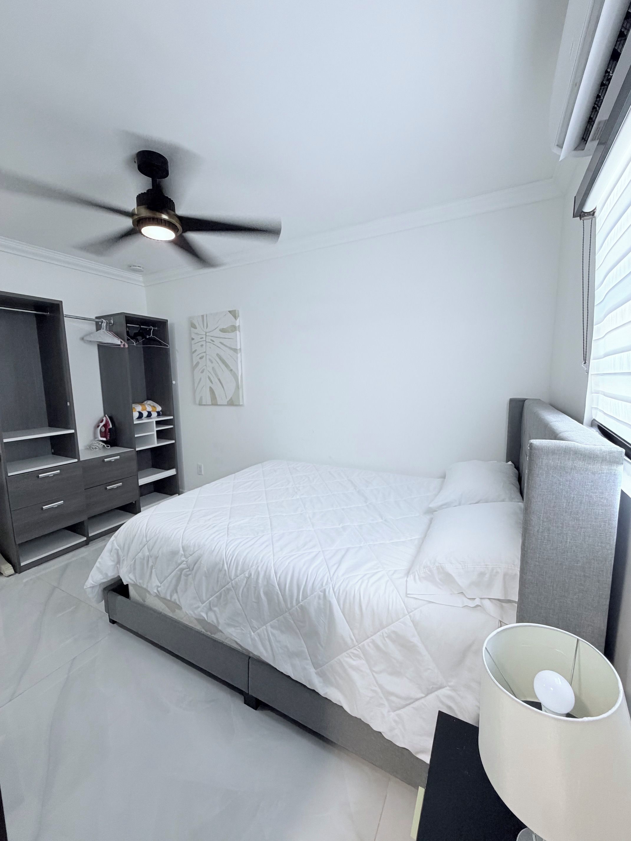 A bedroom with a bed, a wardrobe, a ceiling fan, and a bedside lamp.