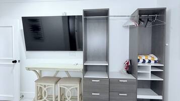 A bedroom with a bed, a desk, a wardrobe, and a hanging clothes rack.