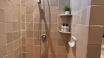 A small, tiled shower stall with a handheld showerhead and a wall-mounted faucet.