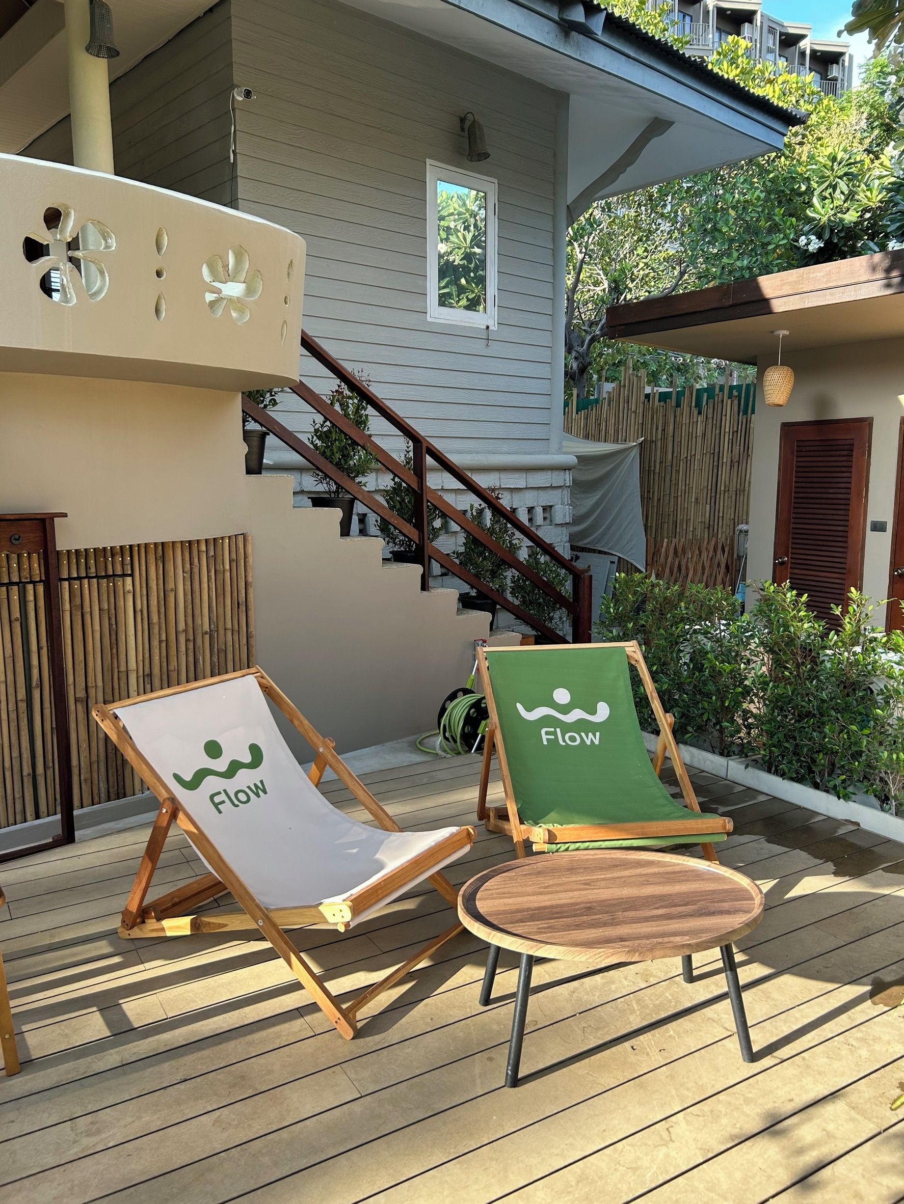 Una terraza de madera con dos sillas reclinables, una con el logotipo 'Flow' y otra con el logotipo 'Flow' y un cojín verde.