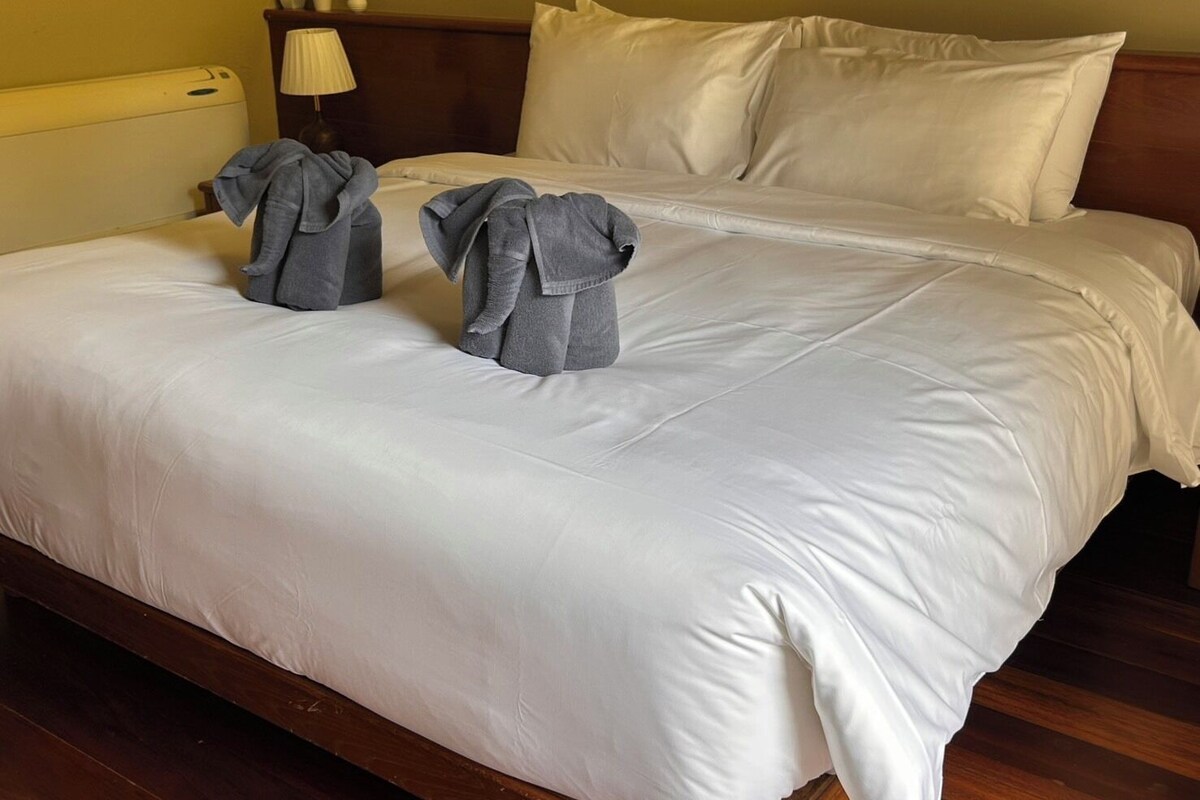 A neatly made bed with white linens and two gray towels placed on the bed.