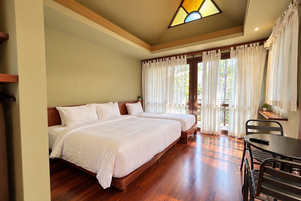 A hotel room with two beds, a dining table, and a view of the outdoors.