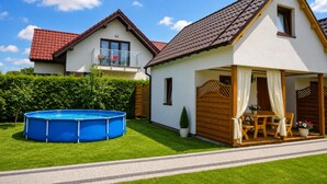 Ein zweistöckiges Haus mit rotem Ziegeldach, einem sichtbaren Balkon und einem Schwimmbad im Vorgarten.