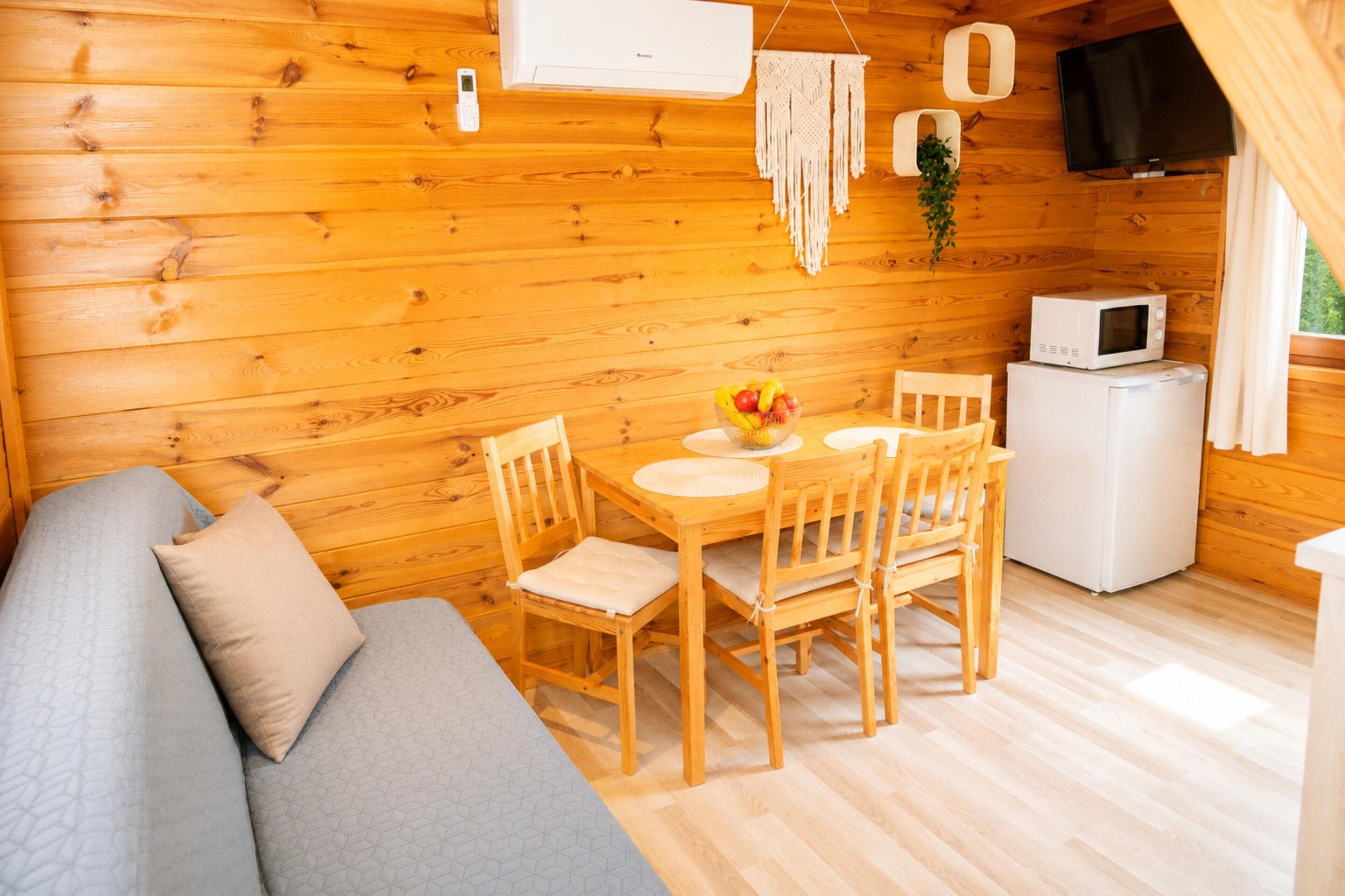 Een houten blokhut van binnen met een eettafel, stoelen, een bank, een televisie en een magnetron.