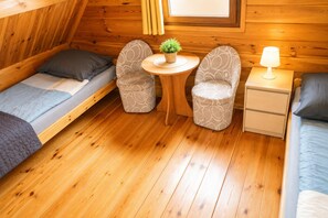 A compact room with two single beds, a small round table with a plant, two patterned chairs, a bedside table with a lamp, and wooden walls. - Holiday Homes for 4 People Near the sea (Kamien Pomorski)