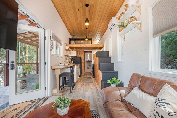 Un interior acogedor con techo de madera, zona de comedor, escalera y sala de estar con sofá de cuero.
