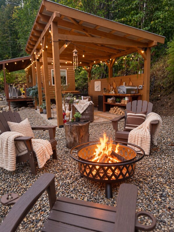 Un patio al aire libre con mobiliario de madera, una chimenea y luces colgantes.