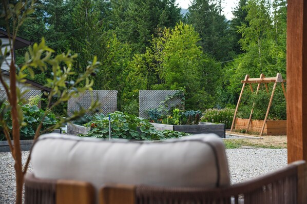 Ein Garten mit erhöhten Beeten, einer Holzschaukel und einer Sitzecke mit Kissen.