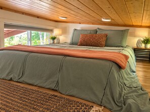 Un dormitorio con una cama grande, techo de madera y vistas al exterior con vegetación.