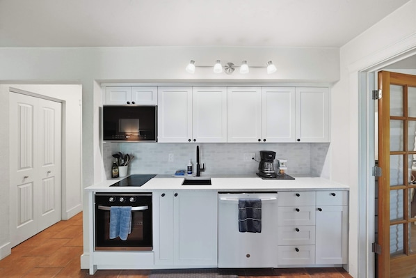 A kitchen with white cabinets, a built-in oven, a microwave, a coffee maker, and a sink. - Cozy Condo by Downtown (Bend)