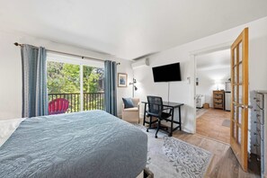 A bedroom with a bed, a desk, a chair, a TV, and a balcony. - Cozy Condo by Downtown (Bend)