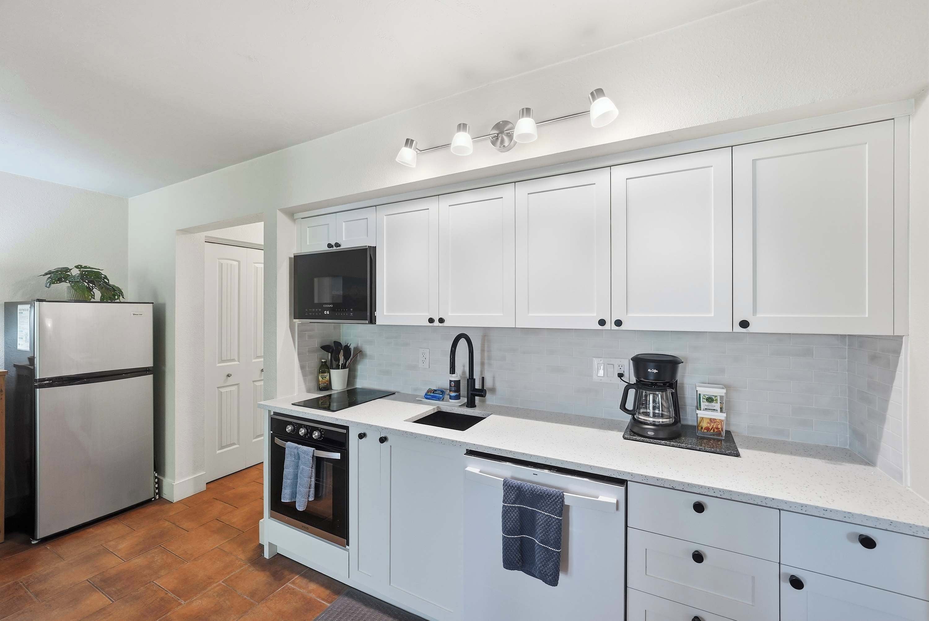 A compact kitchen with white cabinetry, a built-in microwave, a coffee maker, and a dishwasher.