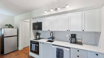A compact kitchen with white cabinetry, a built-in microwave, a coffee maker, and a dishwasher.