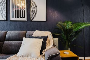 A modern living room with a grey sofa, a white throw blanket, and a large green plant. - Etihad Co-op Live 3-bed Free Parking (Manchester)