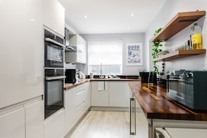 A modern kitchen with white cabinetry, a wooden countertop, and a built-in oven. - Etihad Co-op Live 3-bed Free Parking (Manchester)
