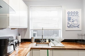A kitchen with a sink, a coffee machine, and a poster on the wall. - Etihad Co-op Live 3-bed Free Parking (Manchester)