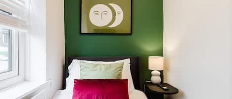 A hotel room with a bed, a nightstand, a lamp, and a wall with a framed picture.