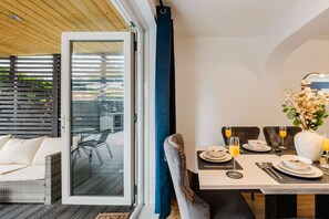 A dining area with a table set for two, a wicker sofa, and a sliding glass door leading to an outdoor deck. - Etihad Co-op Live 3-bed Free Parking (Manchester)