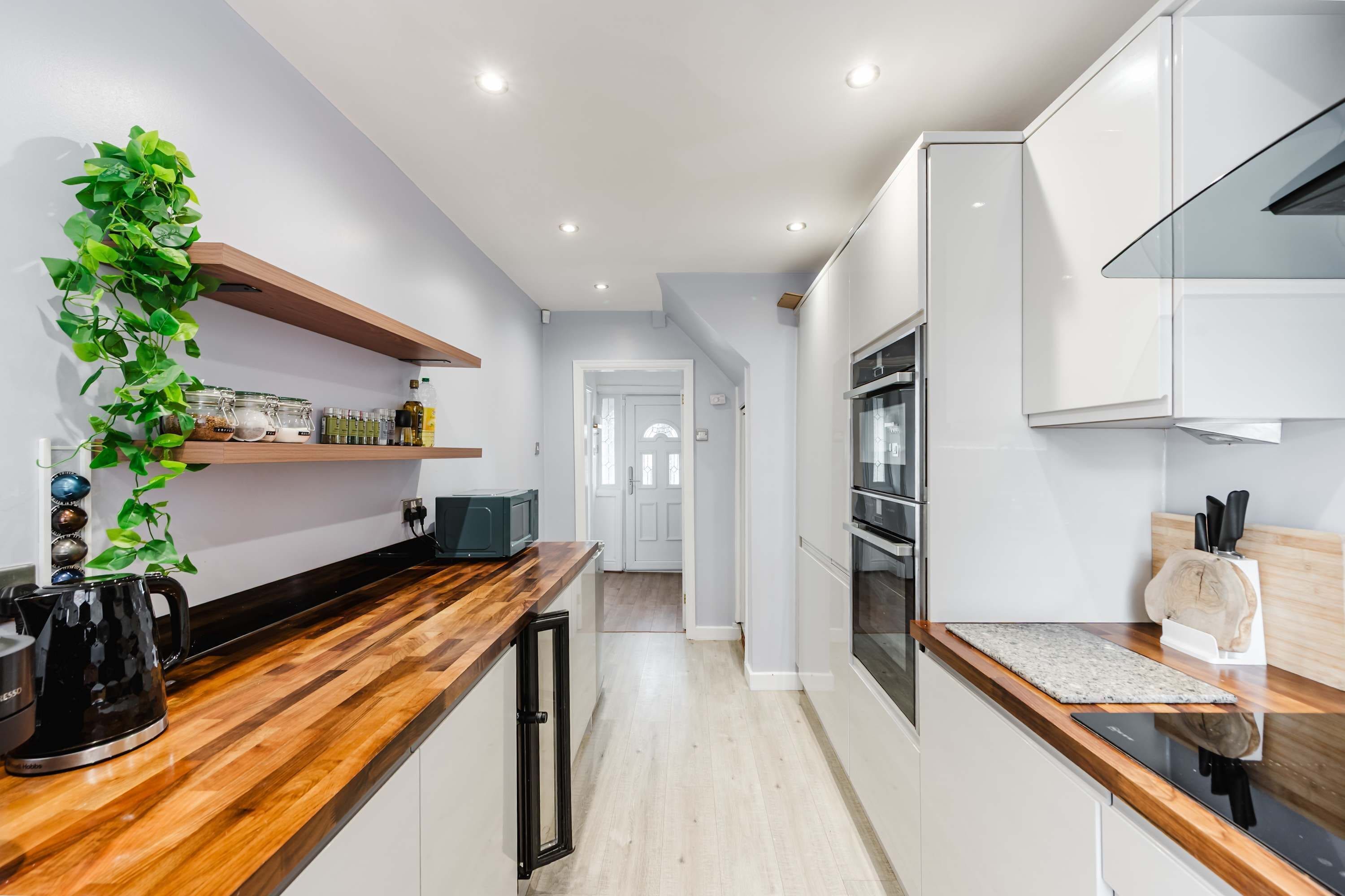A modern kitchen with wooden countertops, built-in appliances, and a plant on the left.