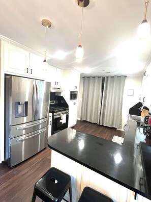 Een moderne keuken met roestvrijstalen apparatuur, een centraal eiland, hanglampen en uitzicht op de woonkamer.