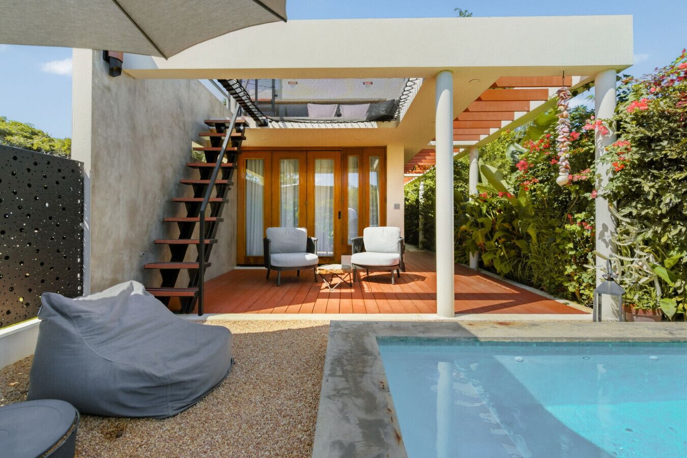 Ein moderner Außenbereich mit Pool, zwei Stühlen, einem Tisch und einer Treppe, die zu einer oberen Ebene führt.