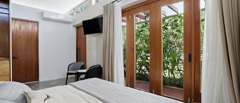 A hotel room with a bed, a desk, a chair, a TV, and a sliding glass door leading to an outdoor area.