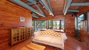 A cozy cabin interior with a wooden floor, a sofa, a wooden cabinet, and a television.