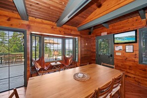 A wooden cabin interior with a dining table, chairs, a television, and a view of the outdoors. - Sunsky at Skyforest - 3bdr (Skyforest)
