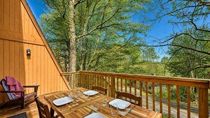 An outdoor wooden deck with a table set for dining, surrounded by trees. - Charming 3-bedroom condo with Pool, Hot Tub, AC  & Games (Beech Mountain)