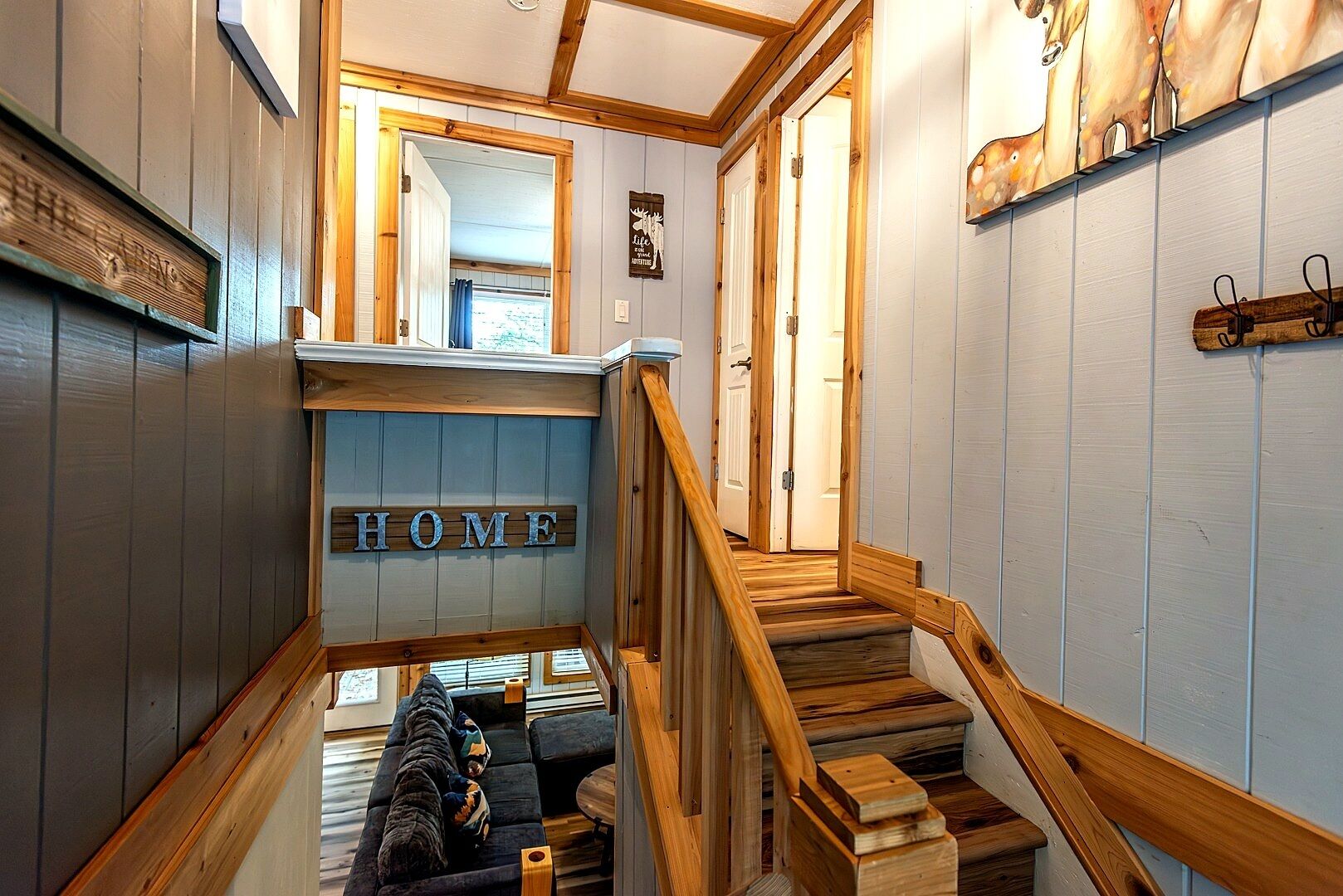 Een houten trap die leidt naar een leefruimte met een bank en een bord waarop 'HOME' staat.