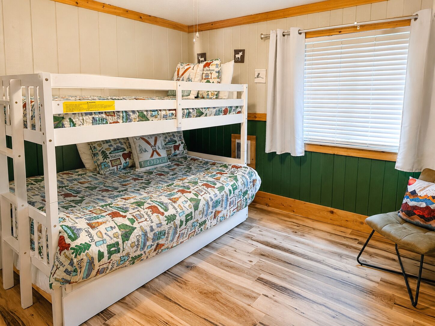 Una cama litera con colcha estampada, una silla, una ventana con persianas y suelo de madera.