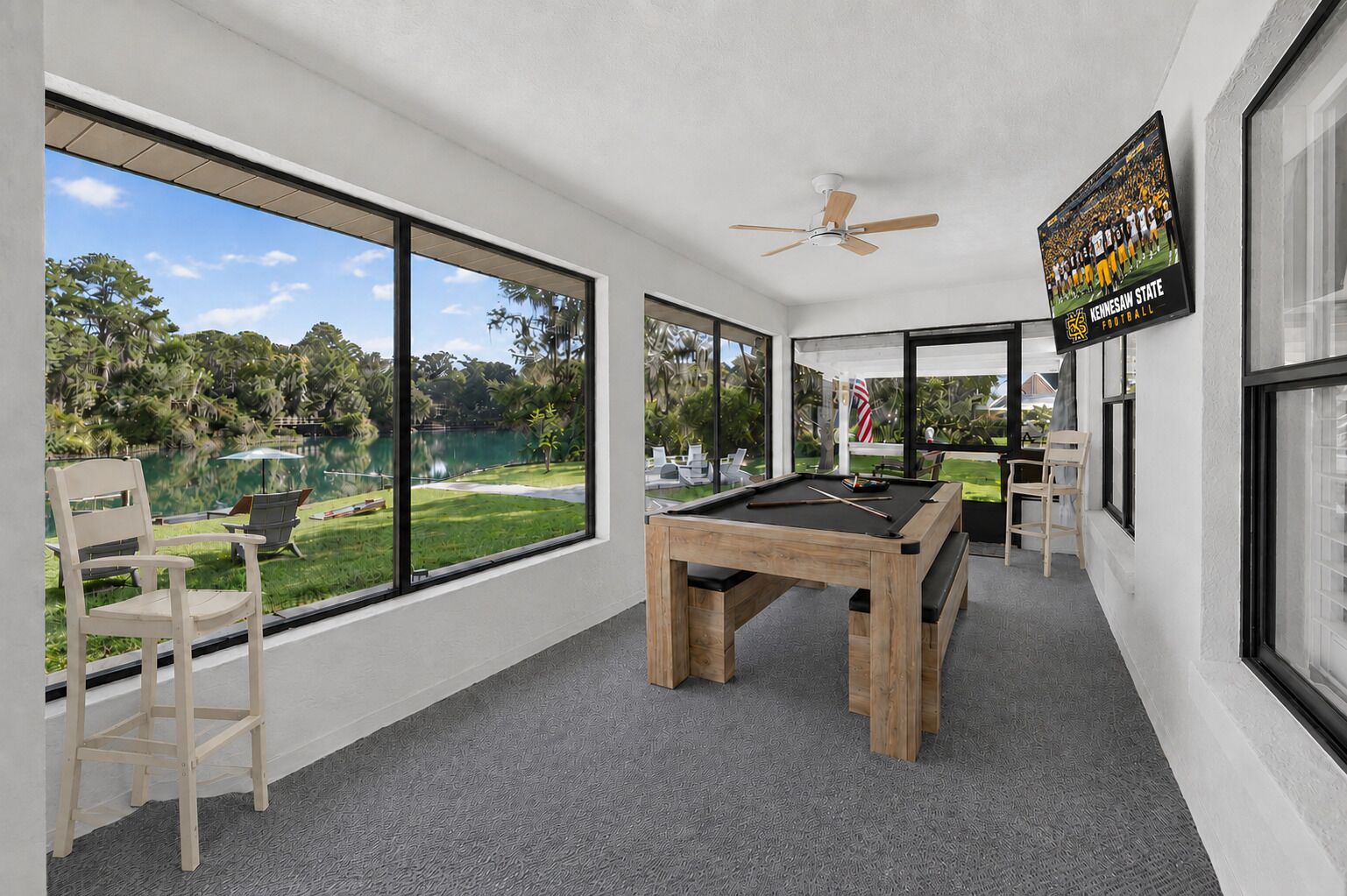 A pool table in a room with large windows overlooking a lake and greenery.