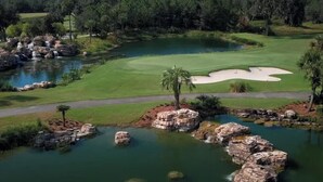 Un campo de golf con un estanque, búnkeres de arena y palmeras.
