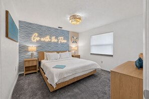 A modern bedroom with a bed, bedside tables, a wall mural, a ceiling light, and a window.