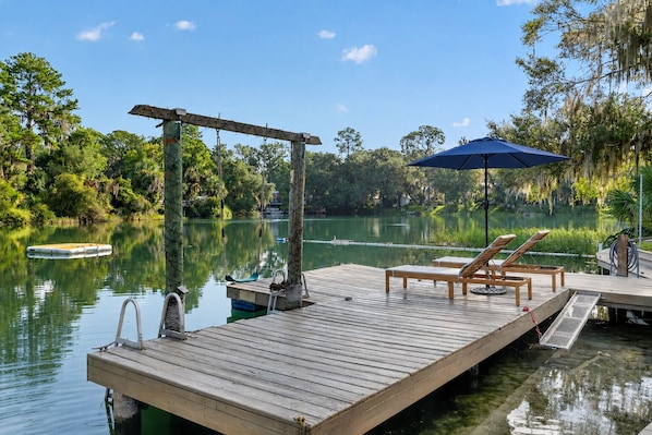 A wooden dock extending into a calm lake, with a swing and lounge chairs on the dock.