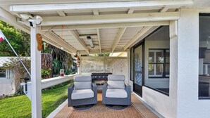 Un patio cubierto con dos sillones grises, una parrilla pequeña y un cerco decorativo.