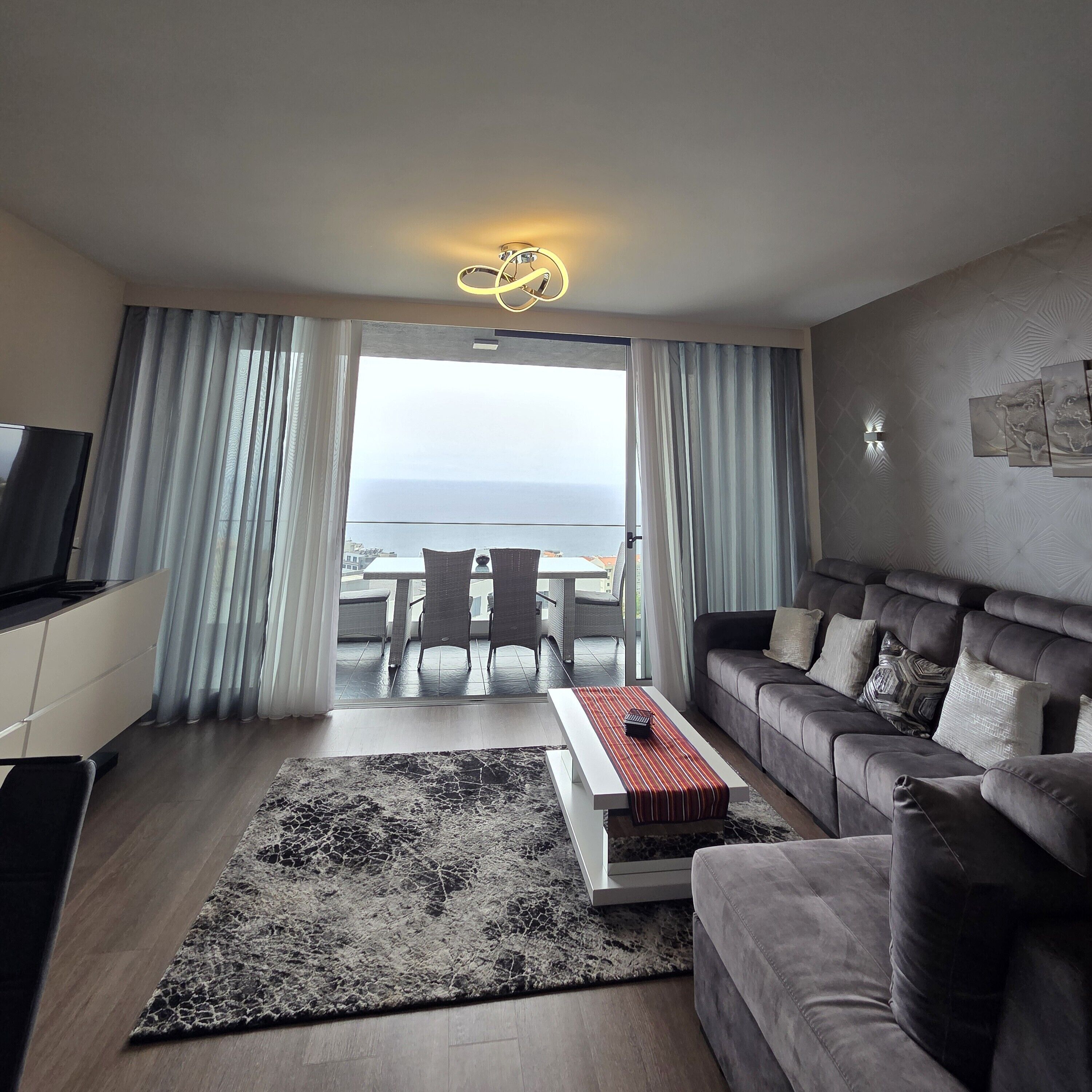 Ein modernes Wohnzimmer mit Sofa, Couchtisch und Fernseher. Ein Balkon bietet Blick aufs Meer.