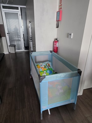 Ein Zimmer mit einem blauen Reisebett, einem Feuerlöscher und einer Tür mit Streifenmuster.