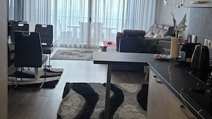 A modern living room with a dining area, a sofa, a coffee table, and a kitchen counter with appliances. - Madeira Mar – Seaview – Top-Floor Apartment with Rooftop Pool-Guest Information (Funchal)
