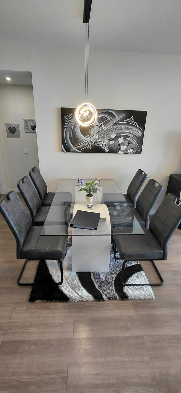 Un espace repas moderne avec une table à plateau de verre entourée de chaises rembourrées, une plante au centre et une œuvre d’art contemporaine accrochée au mur.