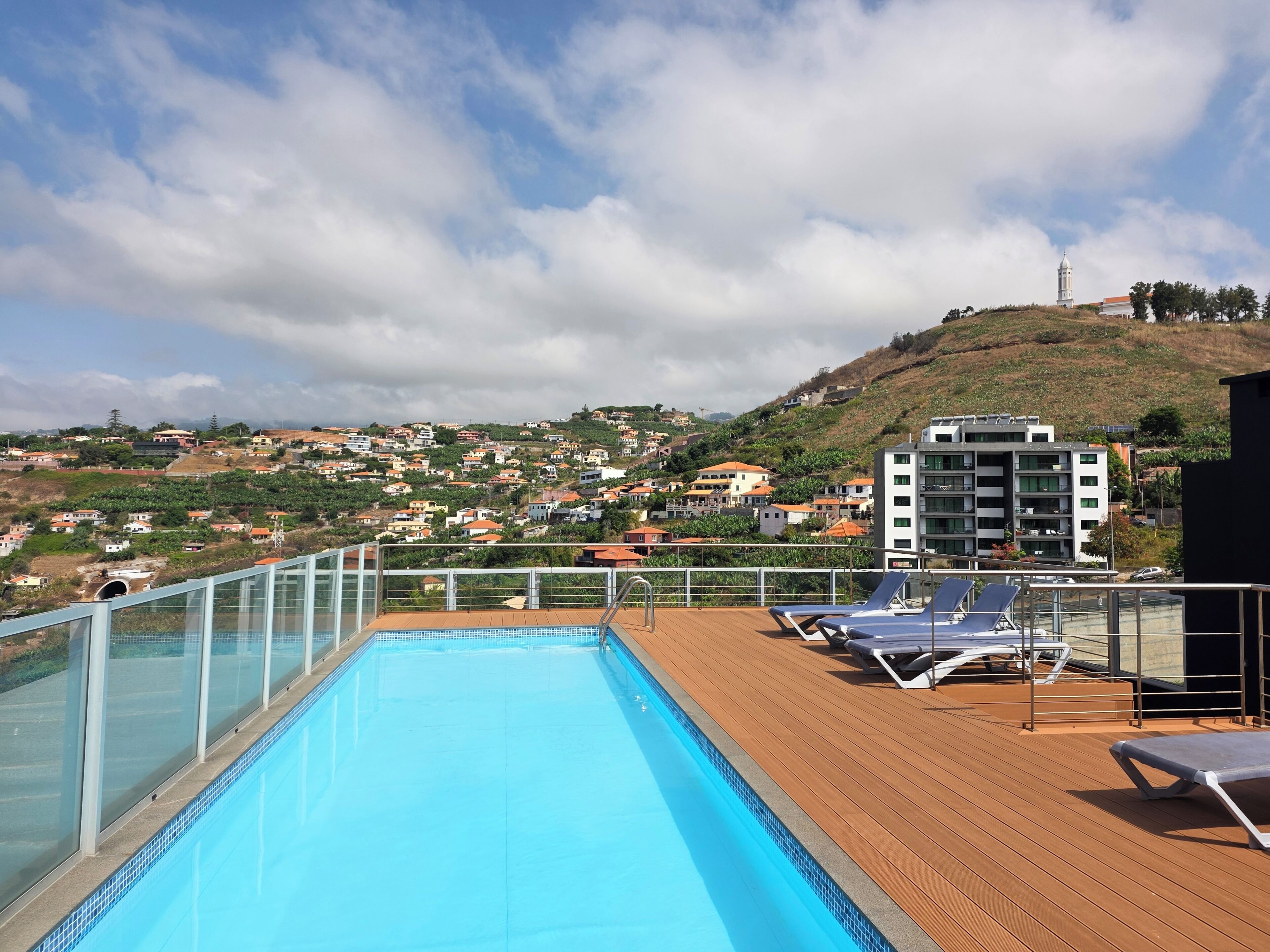 A poolside area with a view of a hillside town, including a modern building and a mosque.