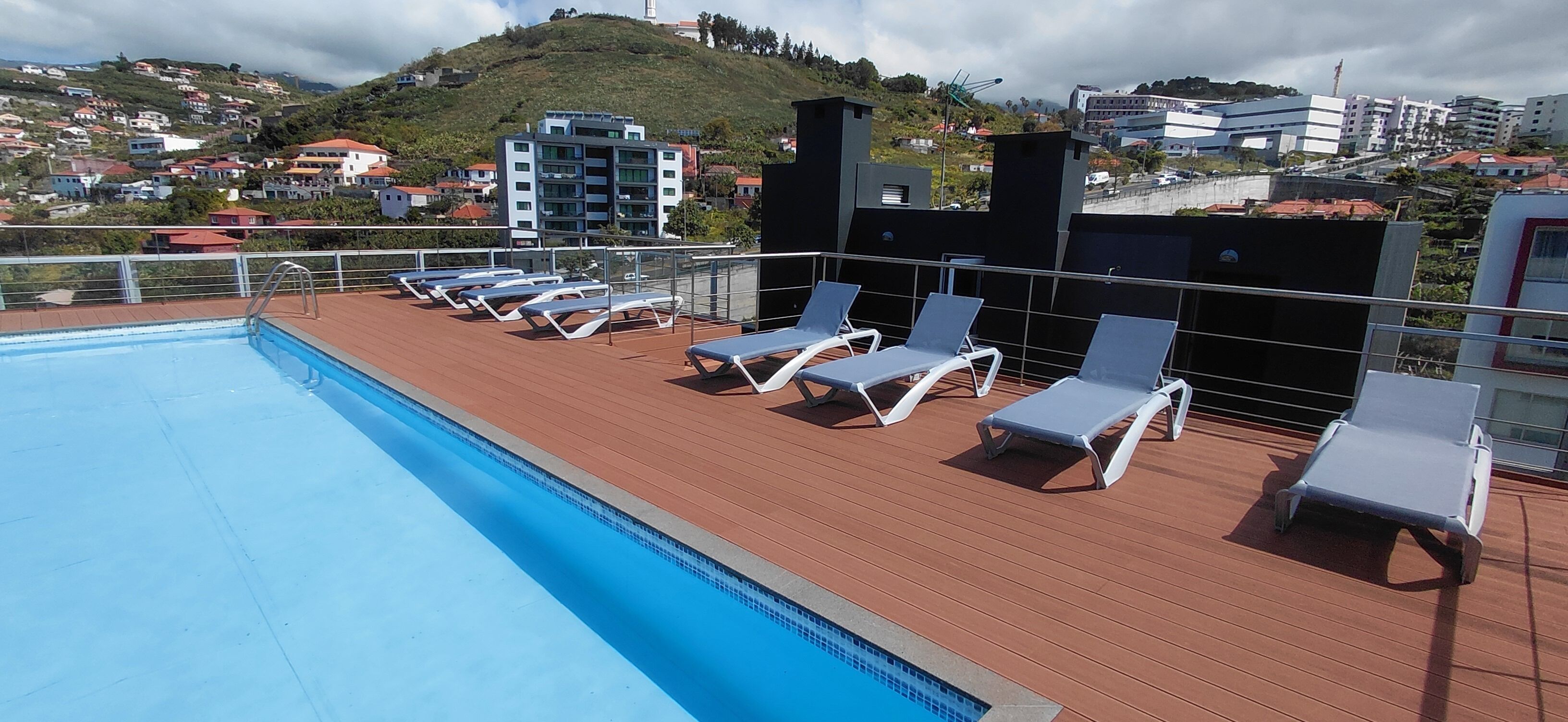 Una piscina en la azotea con tumbonas y vistas a un pueblo en la ladera.