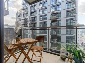 Ein Balkon mit Holztisch und -stühlen, Blumentöpfen und Blick auf ein modernes Gebäude.
