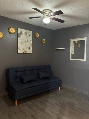A room with a dark-colored sofa, a ceiling fan, wall-mounted decorative plates, and a framed artwork. - Serene and Accessible House Rental in Guaymas, Mexico (San Carlos)